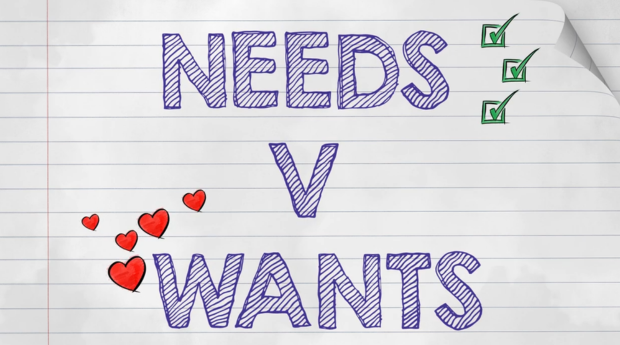 A copybook page with the text 'needs vs wants' written in blue pen