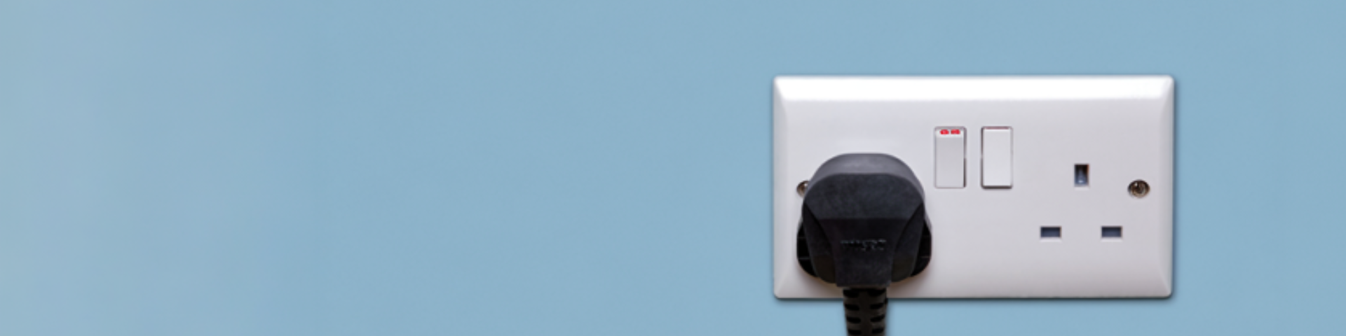 A black plug in a double socket which is switched on, against a blue background