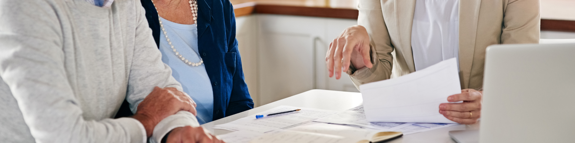 Three people sitting at a table with notepads while one person is showing them something on  a page.