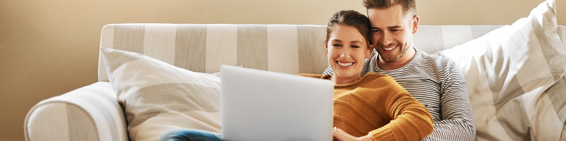 Man and woman sitting on the sofa looking at a laptop screen smiling.