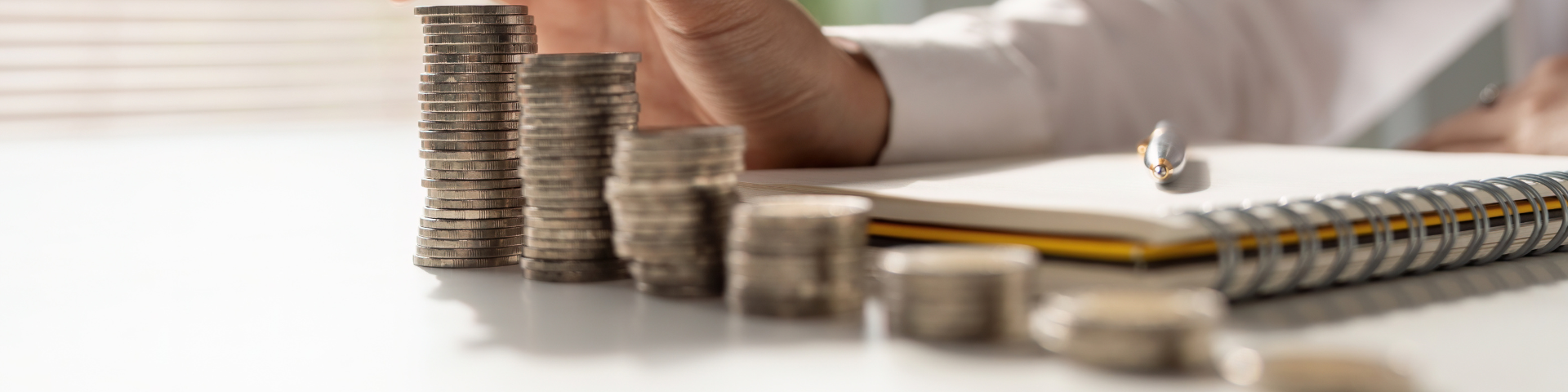 Notebook with pen on top, beside stacks of coins getting larger as they go down the line.