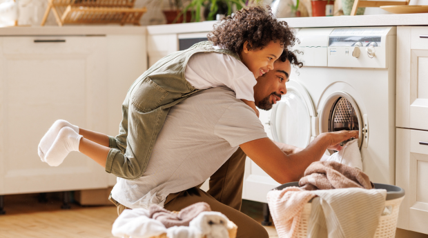 A child and a man play as the man takes laundry out of a tumblr dryer