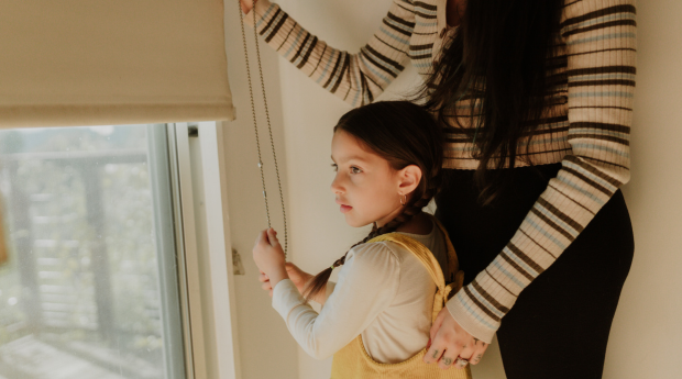 A child and a adult adjust a window blind cord