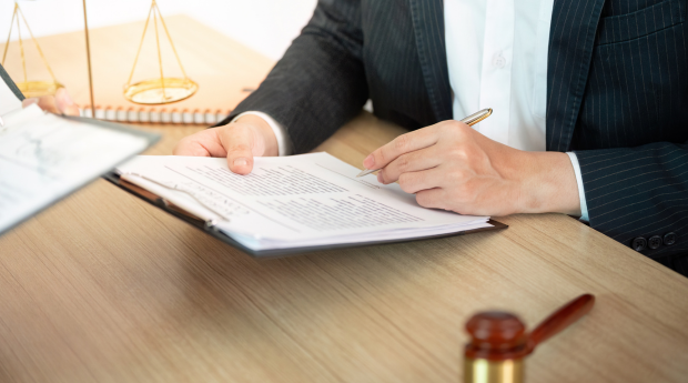 A person wearing a suit reviews a document there is a scale and gavel on their desk
