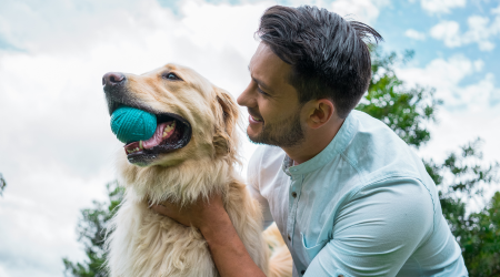 Man smiling beside dog with toy in his mouth.