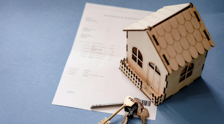 A wooden toy house sits on top of a mortgage bill. Beside it is a set of keys.