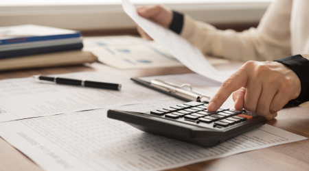 Person using a calculator in one hand and holding up a piece of paper in the other/