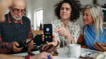 Four people sitting around a table while one holds up her phone showing a call from an unknown number.