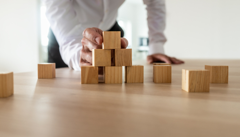 Hand stacking wooden blocks into a pyramid shape.