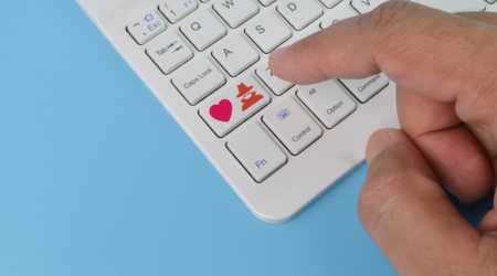 Finger hovering over keyboard button that shows a heart and a man in a hat and coat side by side.