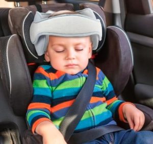Car seat headstraps image 1 A young child asleep in a car seat with a grey head strap on its head.