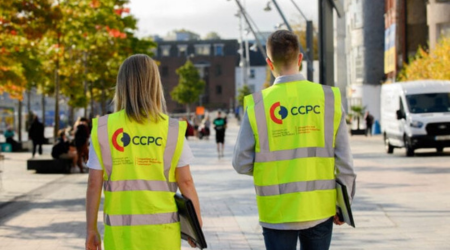 Two people walking down the street wearing CCPC-branded high visibility jackets.
