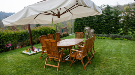 Image shows wooden garden furniture under a large white umbrella in a back garden.