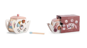 Wooden Activity Teapot A wooden teapot with a pink lid. The teapot features some plant-like illustrations and some small wooden ornaments are attached. To the right is the product's packaging which is maroon in colour.